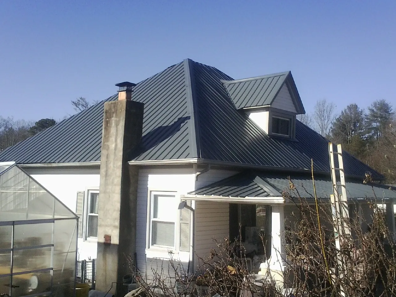 Dark blue standing seam metal roof on a white farmhouse with dormer — Slate & Tile Roof Repair by Roofing Brothers in Pell City