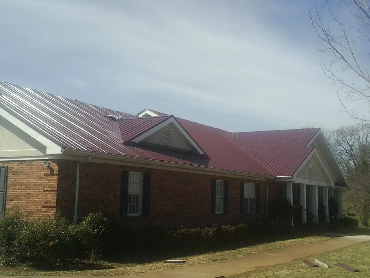 Red metal roof with gabled entries on a long brick building, from a Hail Damage Roof Repair job in Pell City
