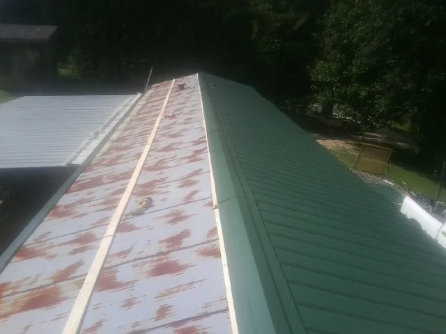 Old rusted panels beside newly installed green metal roofing — Wind Damage Roof Repair by Roofing Brothers in Pell City