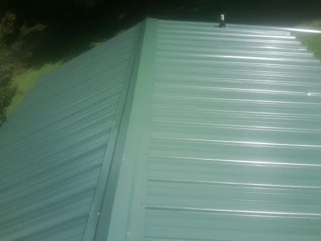 New green metal panels meeting at the ridge of a roof — Flat Roof Repair work by our crew in Pell City