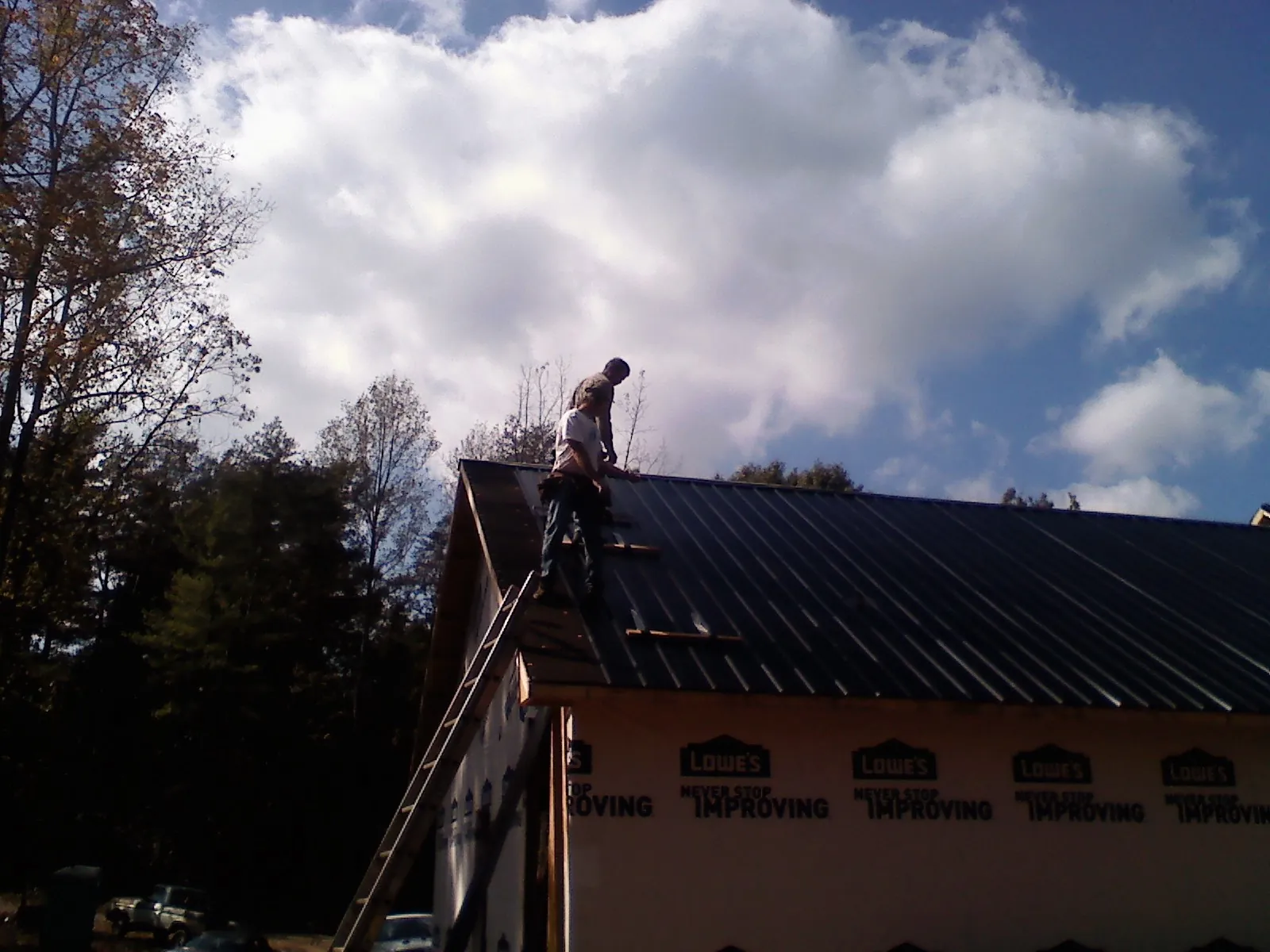 Roofer fastening dark metal panels high against a cloudy sky, from a Roof Inspection job in Pell City